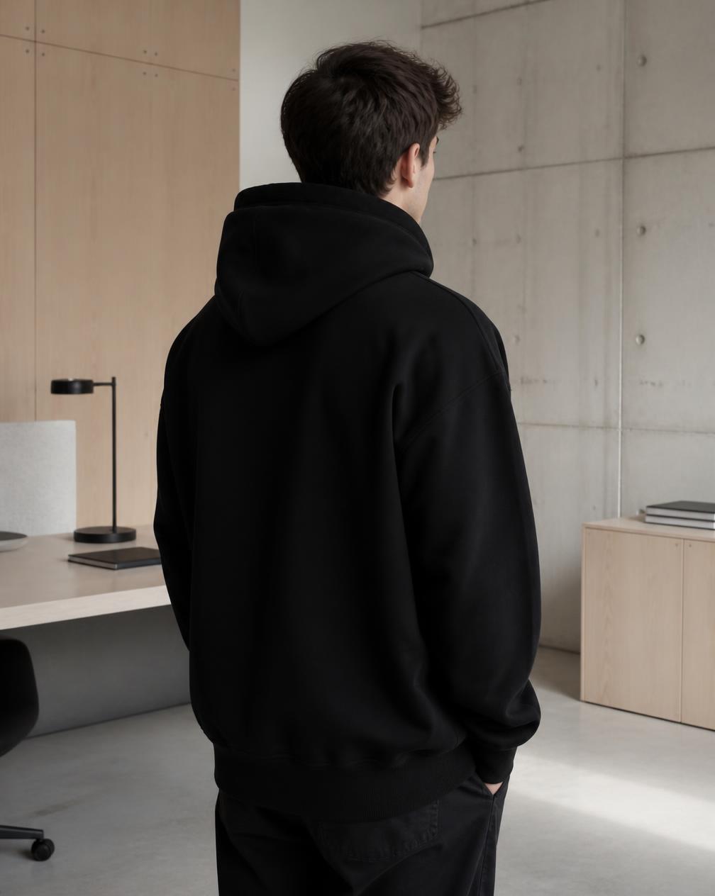 Person in a black heavyweight hoodie in a modern office
